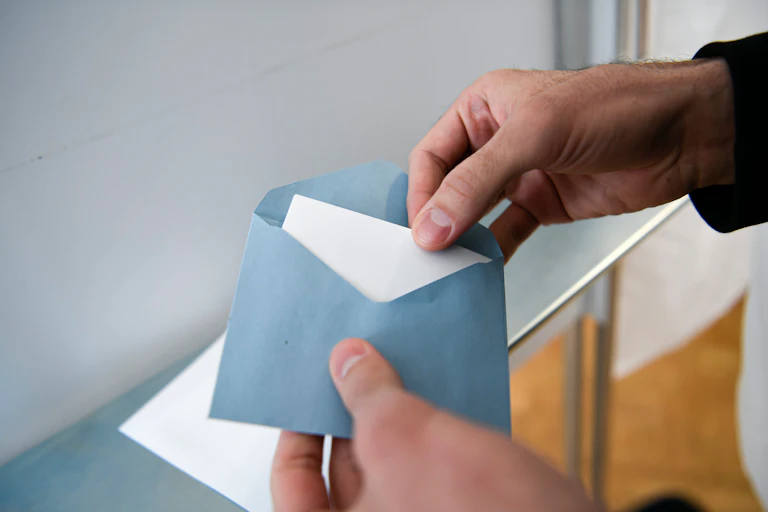 Une personne dans l'isoloir met un bulletin électoral dans une enveloppe.