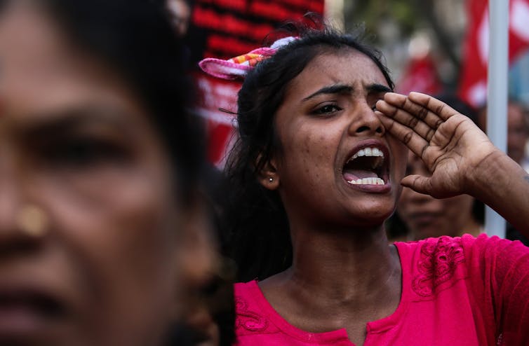 An Indian woman in a pink t-shirt shouting at a protest.