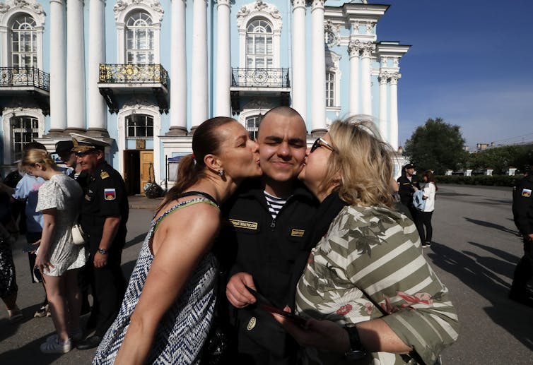Two women kiss a Russian conscript on the cheek.