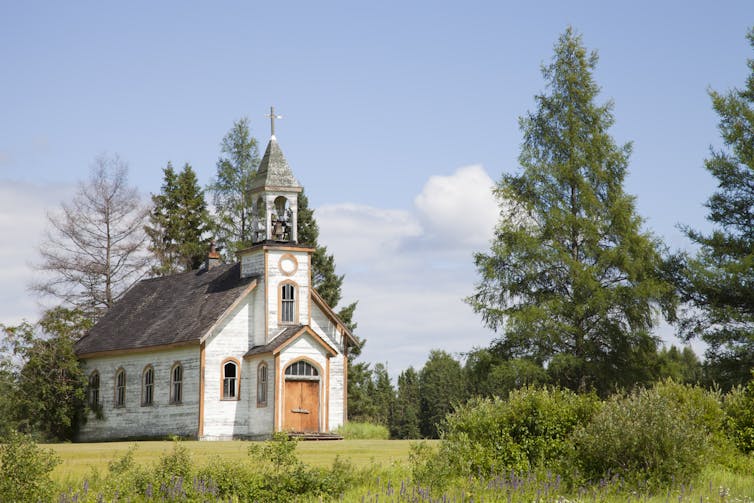 A small white church building in a green field with trees nearby