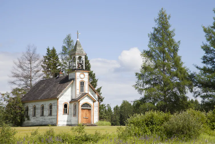 A small white church building in a green field with trees nearby