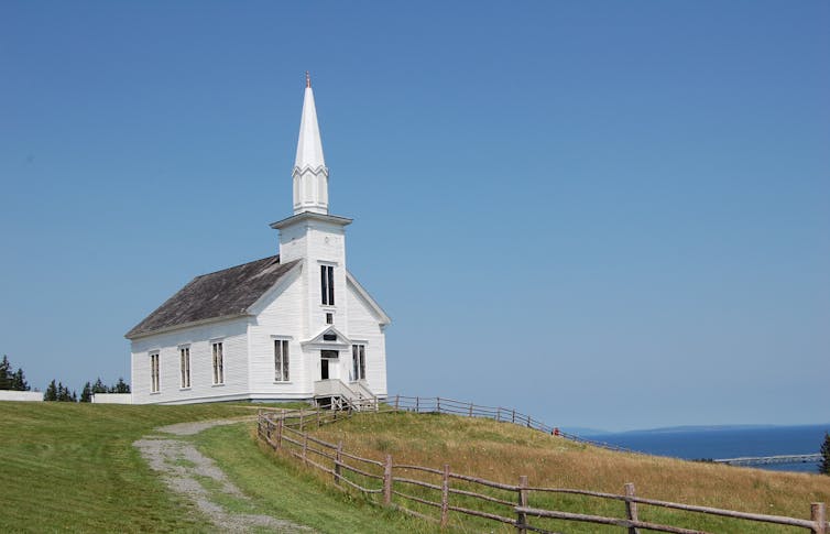 A small white church on a hill overlooking a body of water