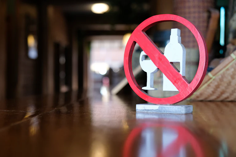 A sign with a bottle and glass with a red line across them
