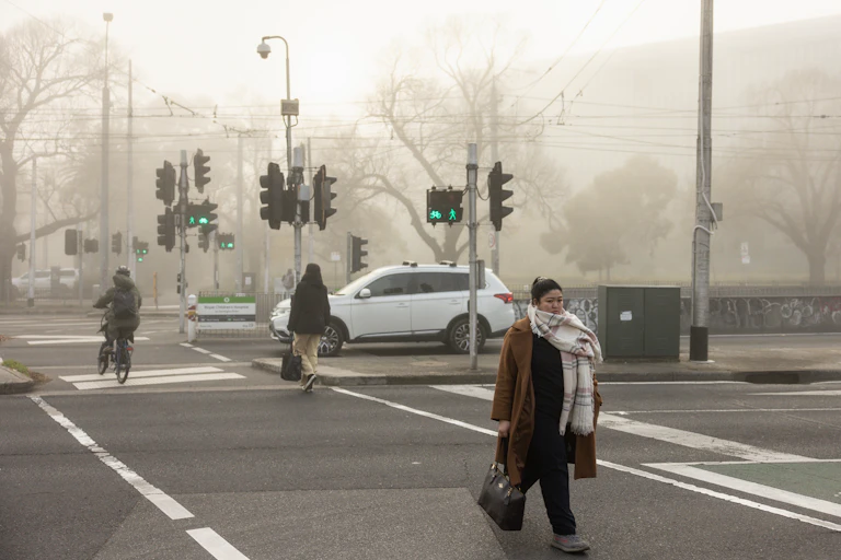 A woman in a heavy long coat and thick scarf crosses the street on a chilly morniing