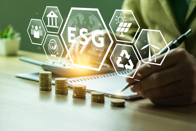 The acronym ESG is seen floating about an image of a hand writing in a notebook, with various business-related symbols floating alongside it
