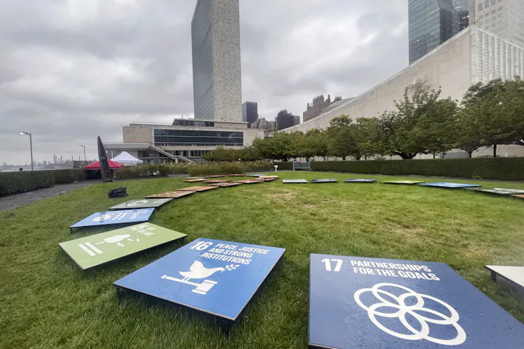 Colourful titles with symbols and text depicting the United Nations’ Sustainable Development Goals are displayed on a grassy field with a building seen in the background