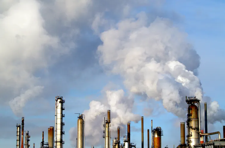 Smoke billows upward from a number of oil refinery chimneys