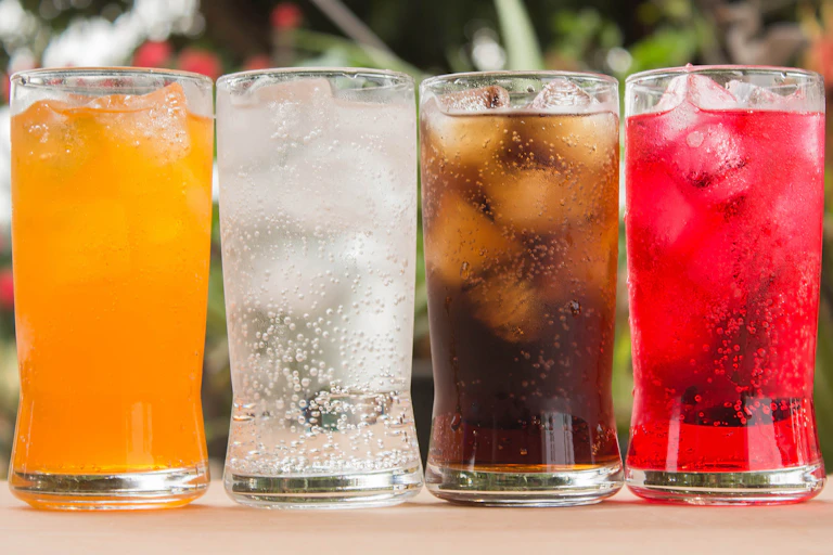 Four glasses of different coloured soft drinks lined up in a row.