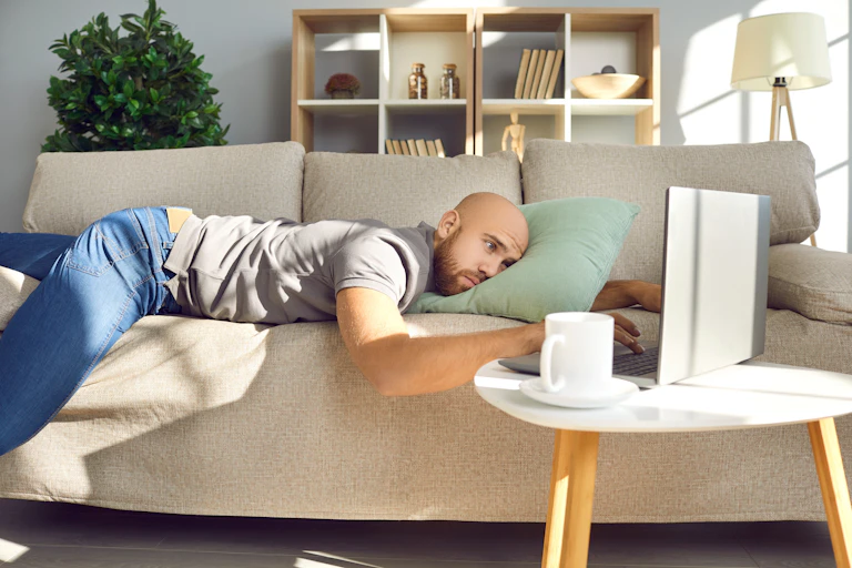 Man lying on couch looking at laptop