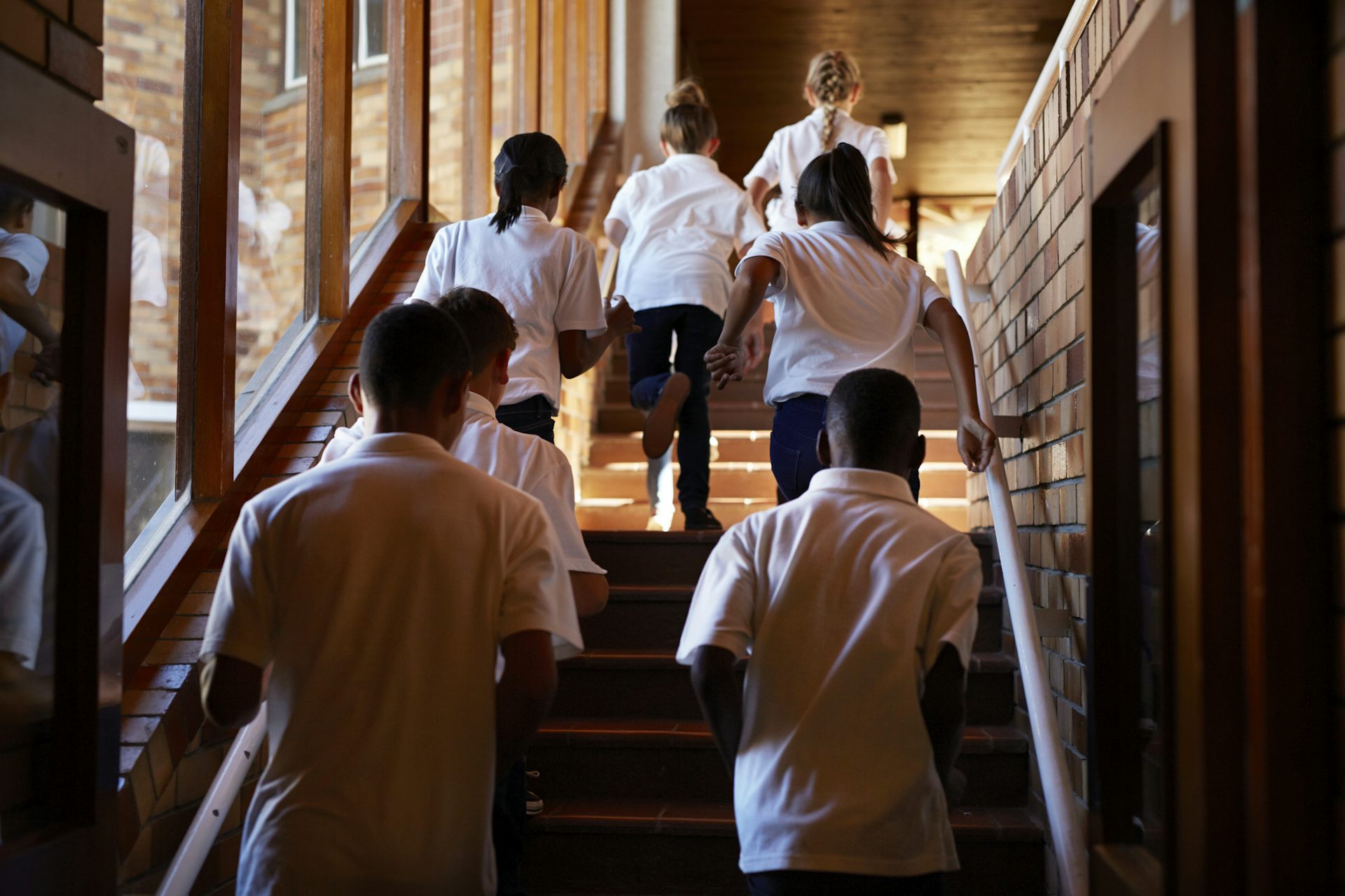 Students in white shirts and dark trousers climb an internal staircase.