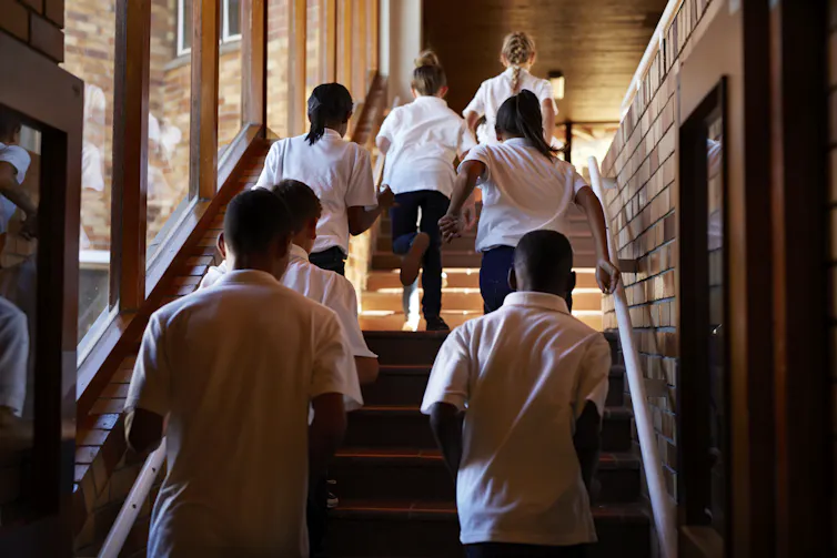 Students in white shirts and dark trousers climb an internal staircase.