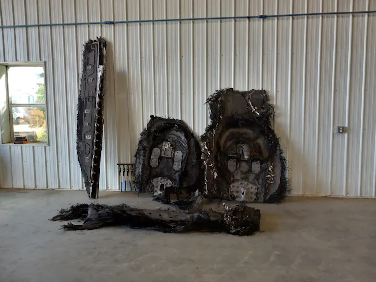 five large burned out husks of metal are leaned against a barn wall