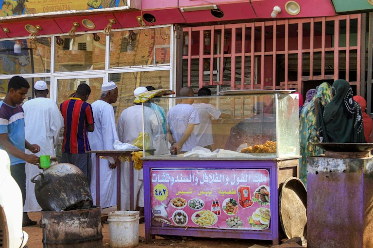 A queue forms in front of a metal grille shop window