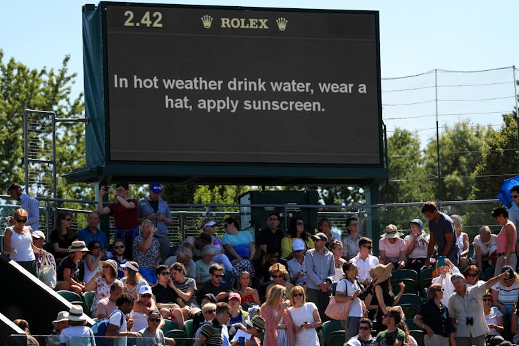 big black sign with hot weather warming, crowds of people below in summer clothing, blue sky