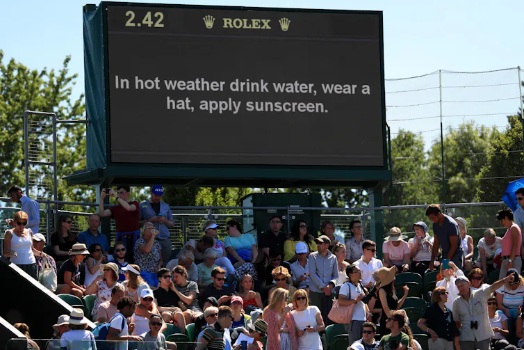 big black sign with hot weather warming, crowds of people below in summer clothing, blue sky