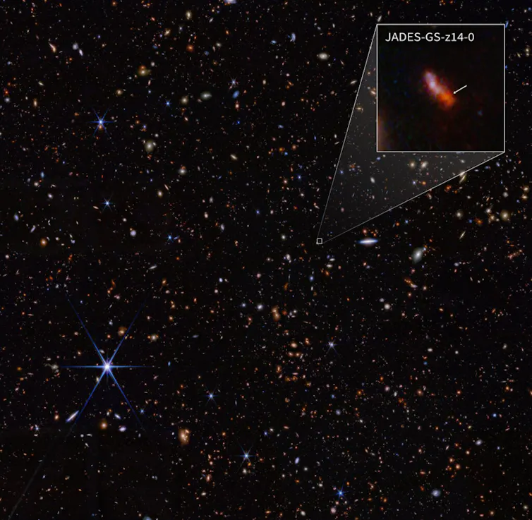 an image of a galaxy showing white flecks on a dark background with an inset showing a reddish-purple elongated blob