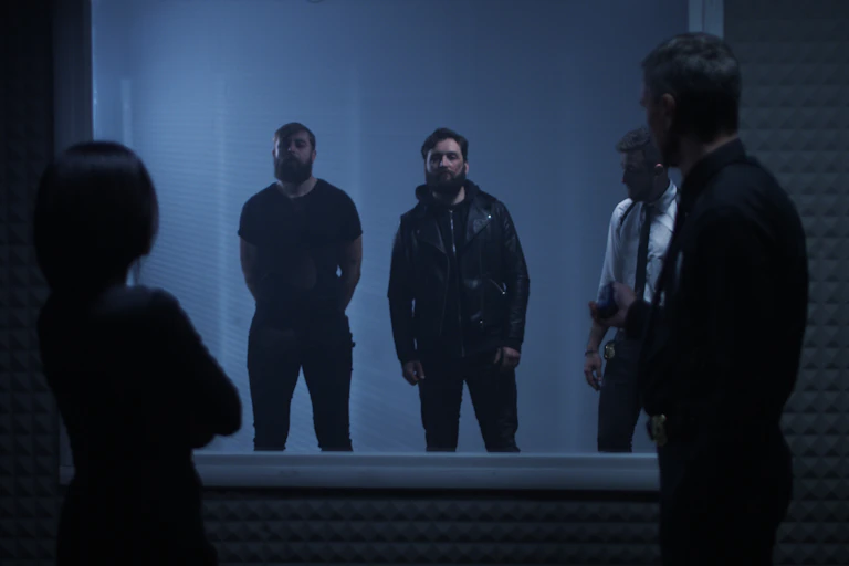 Two people stand on one side of a window examining three men on the other side of the window