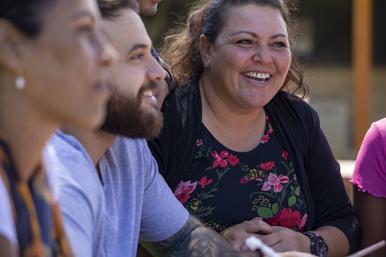 Three people sit around a table, talking and smiling.