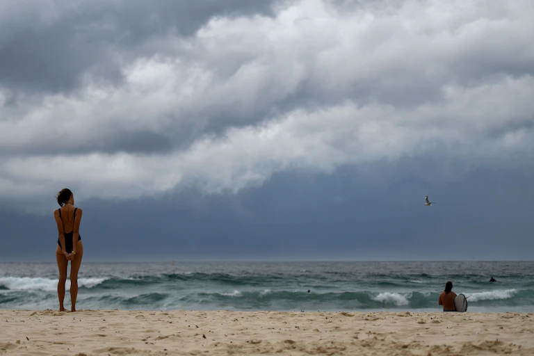 Storm clouds roll in over Bondi Beach in Sydney, as a swimmer stands on the sand looking out at the sea