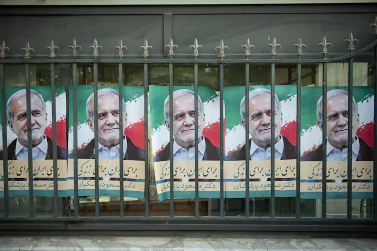 Posters for Iranian presidential candidate Massoud Pezeshkian behind the bars of an iron fence.