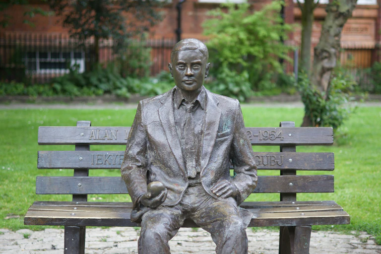 Statue d'Alan Turing assis sur un banc, une pomme dans la main, à Manchester.