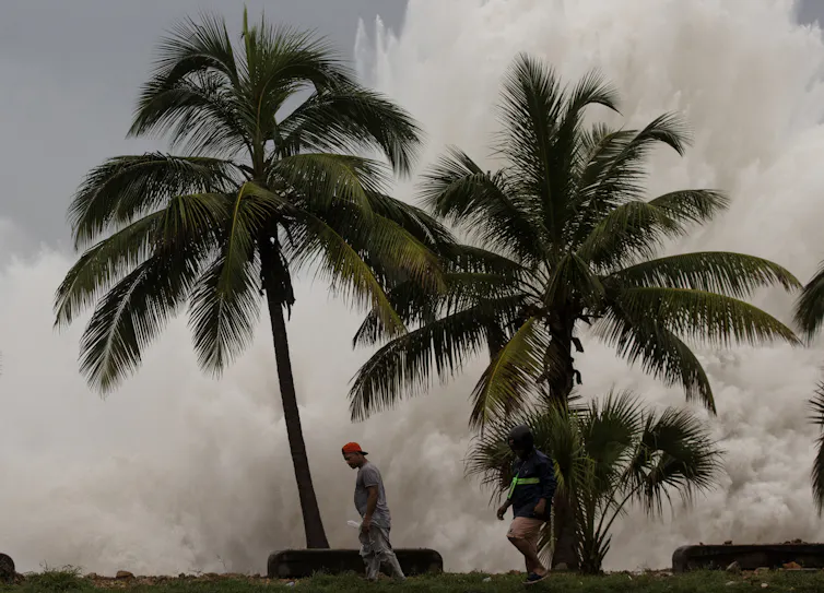 Man walks in front of large sea spray