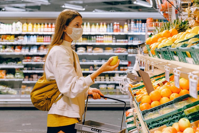 A woman wearing a mask selecting fruit in a grocery store.