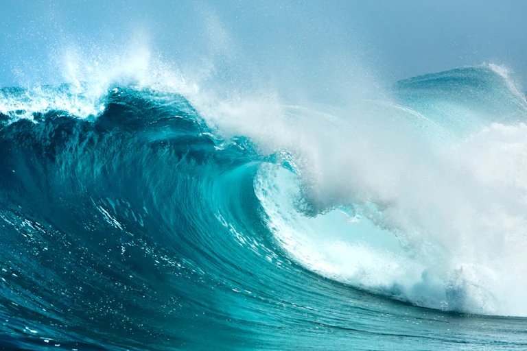 big blue wave crashing, white sea spray, blue sky