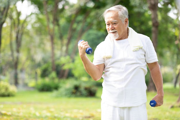 An older man performs a bicep curl in the park.