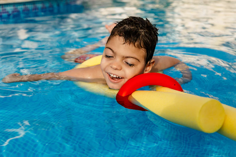 A boy floating in a pool on yellow pool noodle