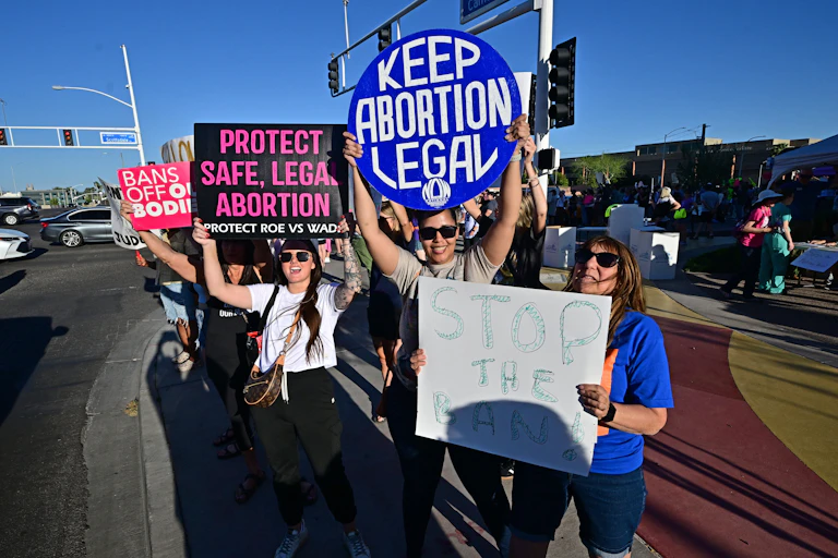 A group of women hold abortion-rights protest signs at a busy intersection.