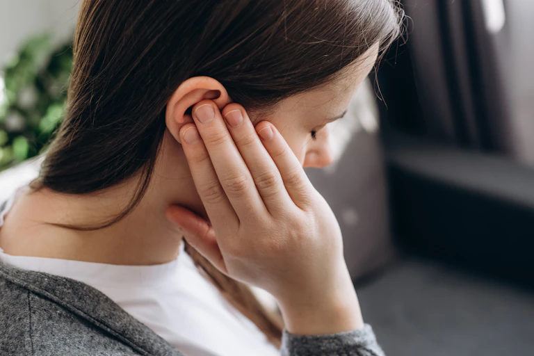 woman holds hand to ear, has eyes closed