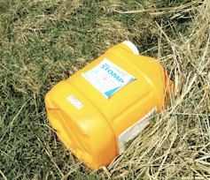 An orange plastic container that used to hold pesticides on grass