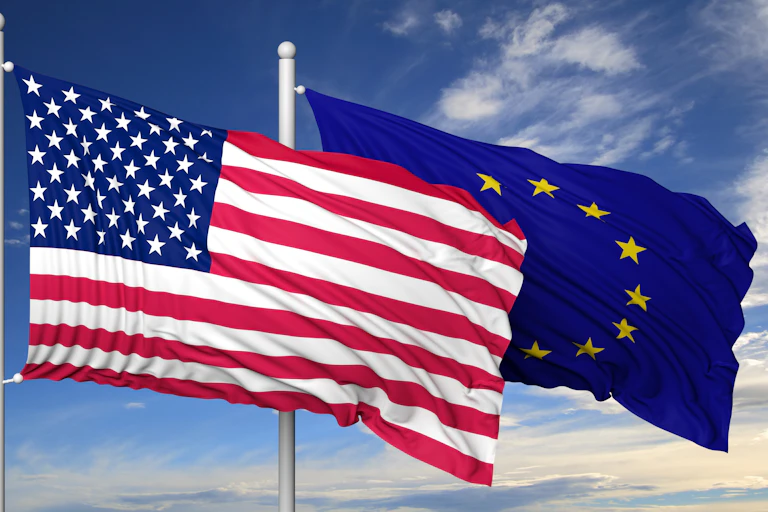 les drapeaux des USA et de l'Union européenne flottent sur un ciel bleu.