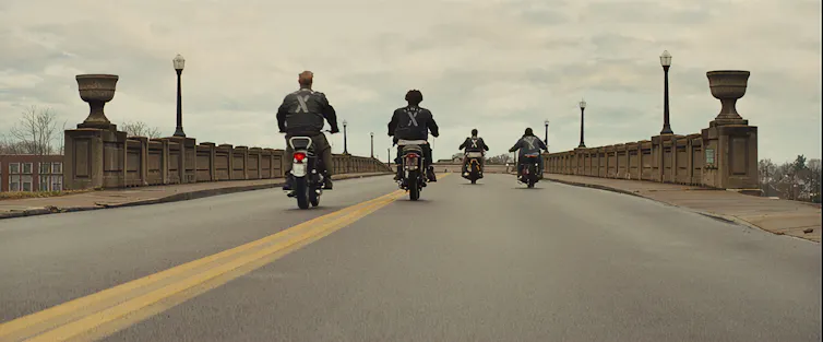 Riders going over a bridge on motorcycles.
