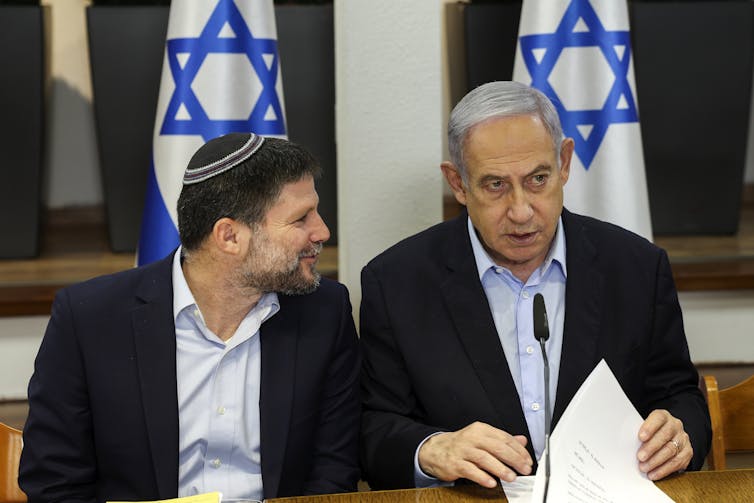 Netanyahu and Bezalel Smotrich sat in discussion in front of Israeli flags.