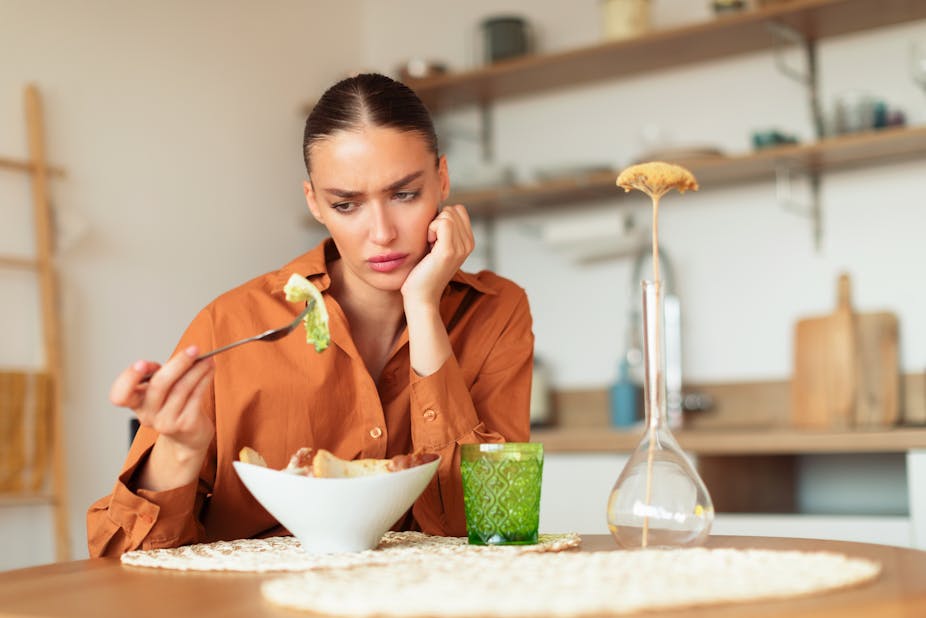 A young woman looks in confusion at a piece of lettuce on her fork.