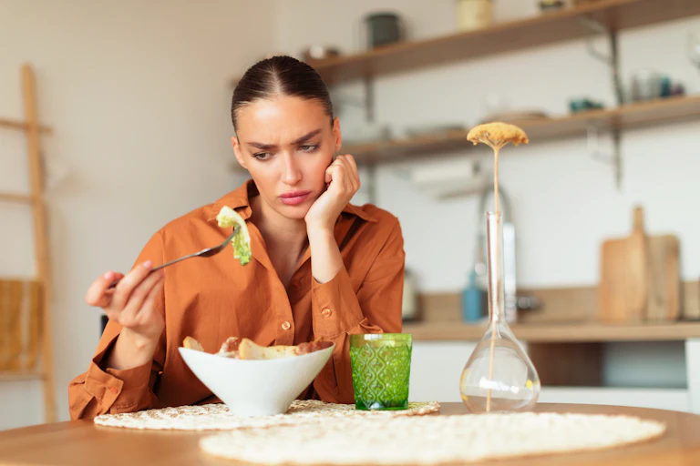 A young woman looks in confusion at a piece of lettuce on her fork.