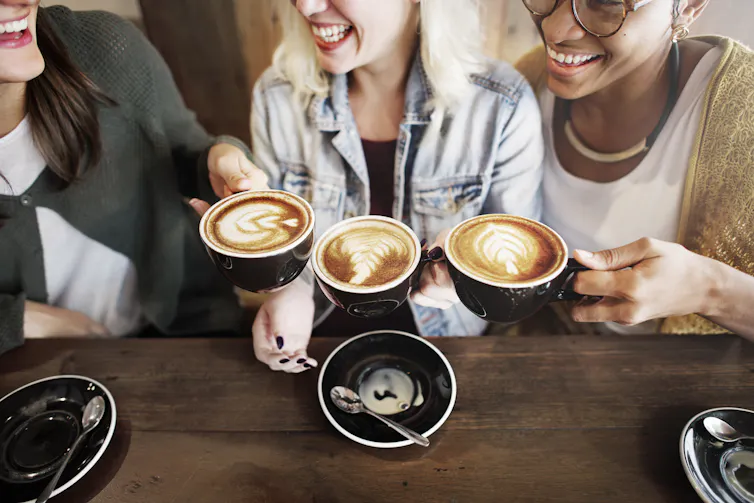 Women sit on a coffee shop and raise their mugs