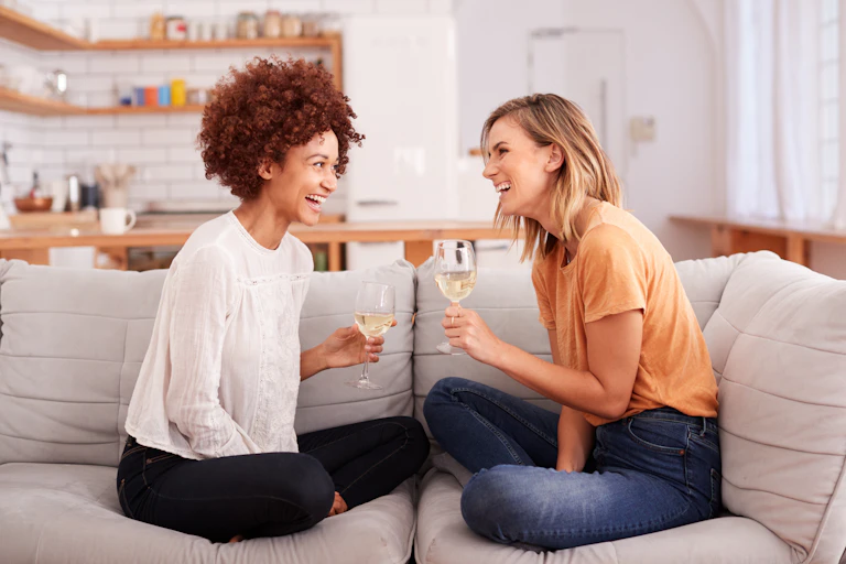 Two women sit on a sofa talking and drinking wine