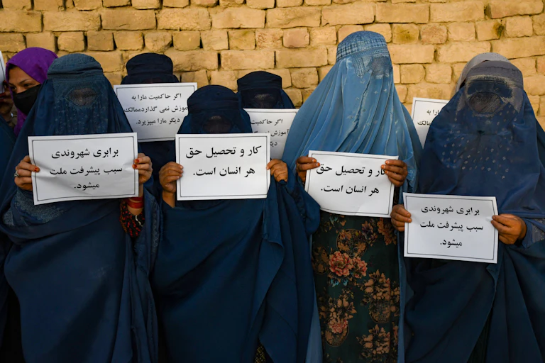Women wearing robes and veils covering them entirely hold up posters
