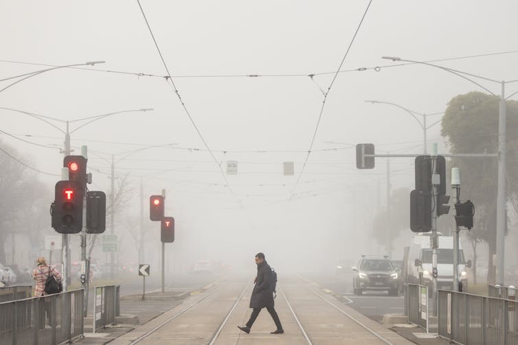 A bundled-up man crossing tram lines in fog.