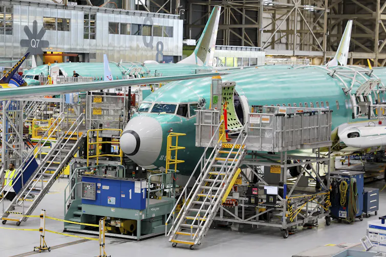 Airplanes seen inside a factory. A set of stairs leads up to the open front door of each plane.