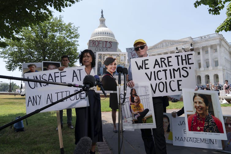 Un grupo de personas sostiene carteles que dicen 'Somos la voz de las víctimas' y 'Inseguro a cualquier altitud' mientras se encuentran frente al Capitolio de los Estados Unidos, un edificio blanco de estilo neoclásico.