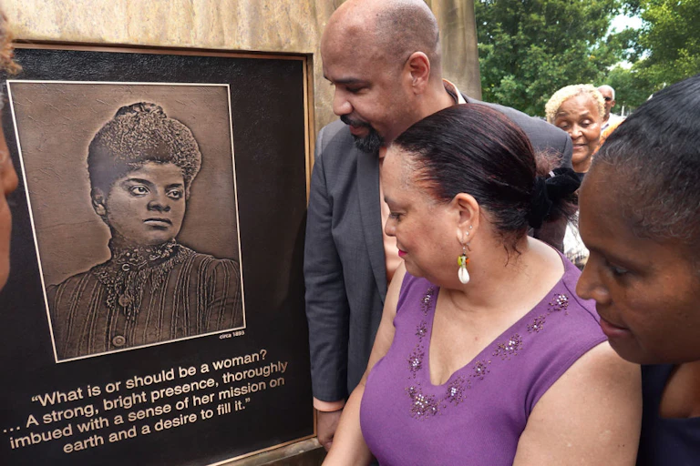 A handful of people gaze at a plaque with a woman's portrait and a quote beneath it.