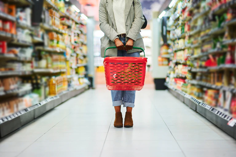 Supermarket aisle, woman legs and basket for shopping in grocery store.