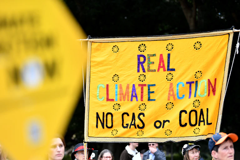 A large yellow protest sign reading real climate action no gas or coal