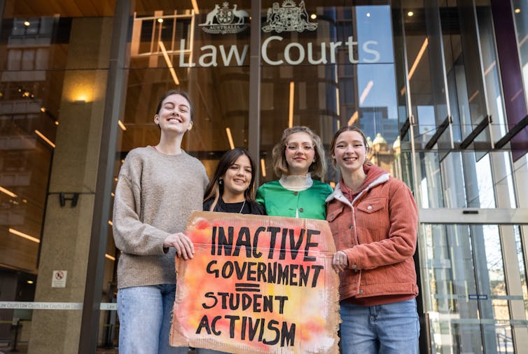 Four teenage girl stand outside a court with a sign than says inactive government equals student activism