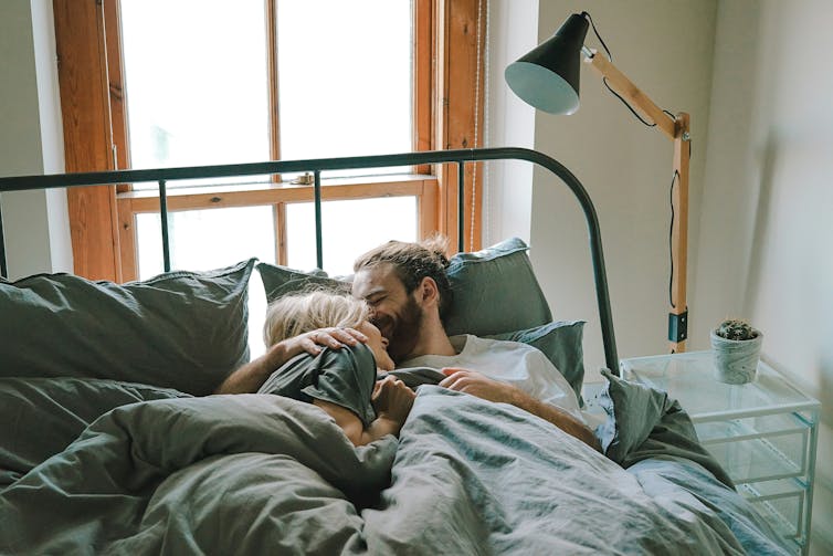 Two people cuddle in bed.