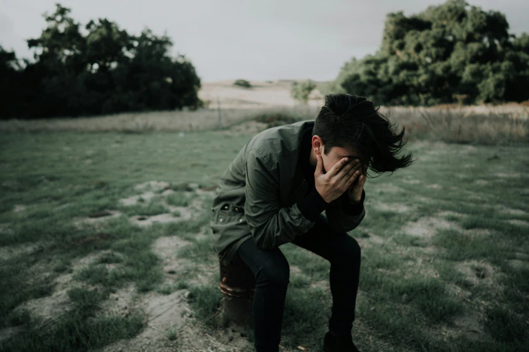 Man sitting on stool, covering his eyes